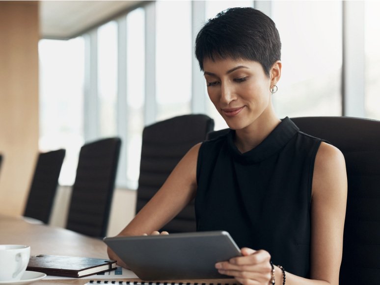 A woman sits at a table using a tablet computer.