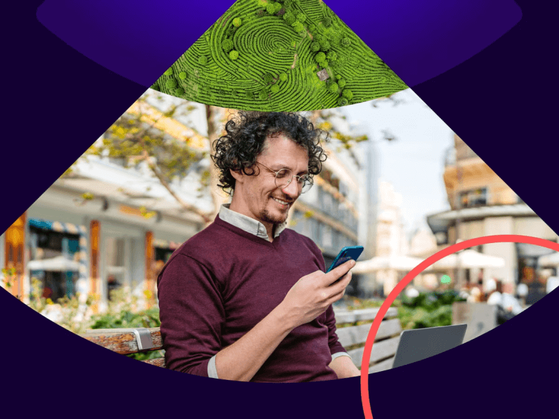 Man sitting outside on a park bench looking at his mobile phone while on a laptop