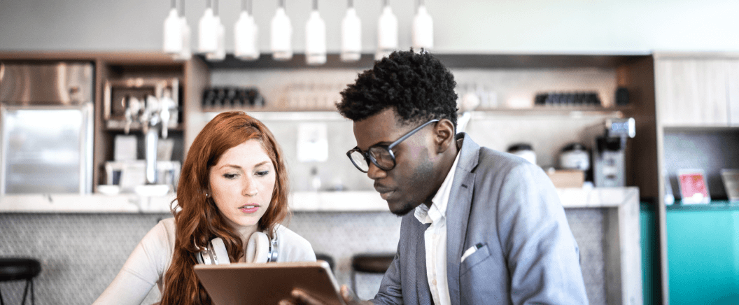 Two individuals collaborate over a tablet in a modern café, surrounded by stylish decor and soft lighting.