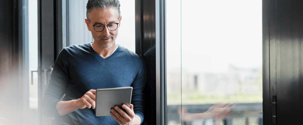 Man with glasses next to a window scrolling on a tablet